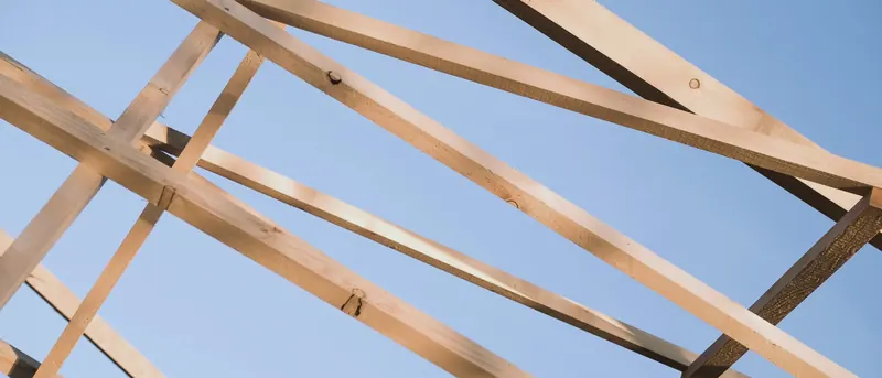 Chevrons et pièces de charpente en bois clair qui se croisent sur un ciel bleu