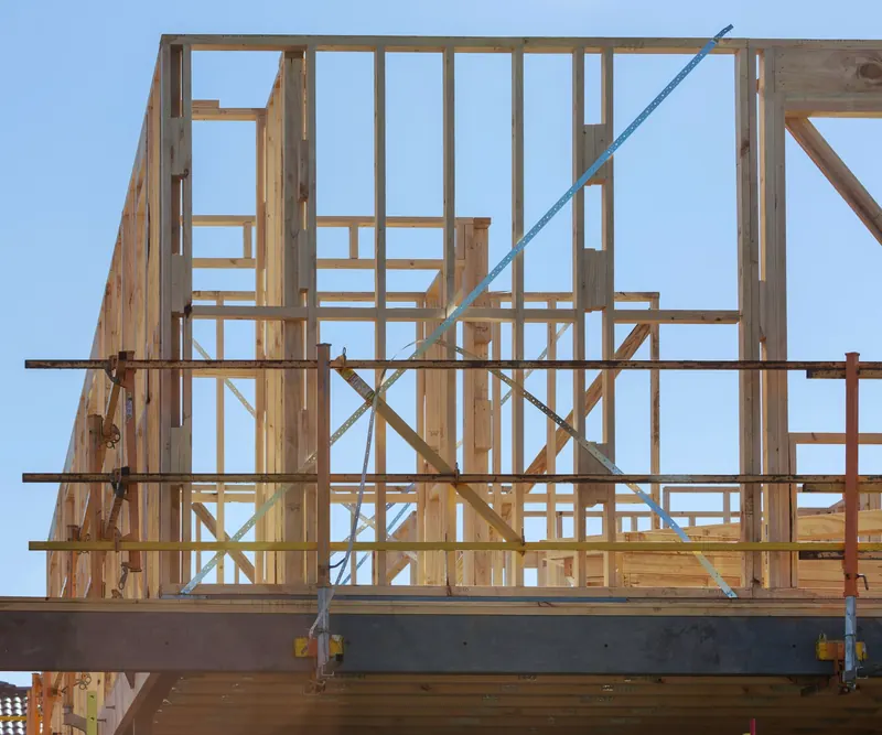 Étage en ossature bois en cours de montage au-dessus d'une poutre métallique, derrière un échafaudage, sur fond de ciel clair