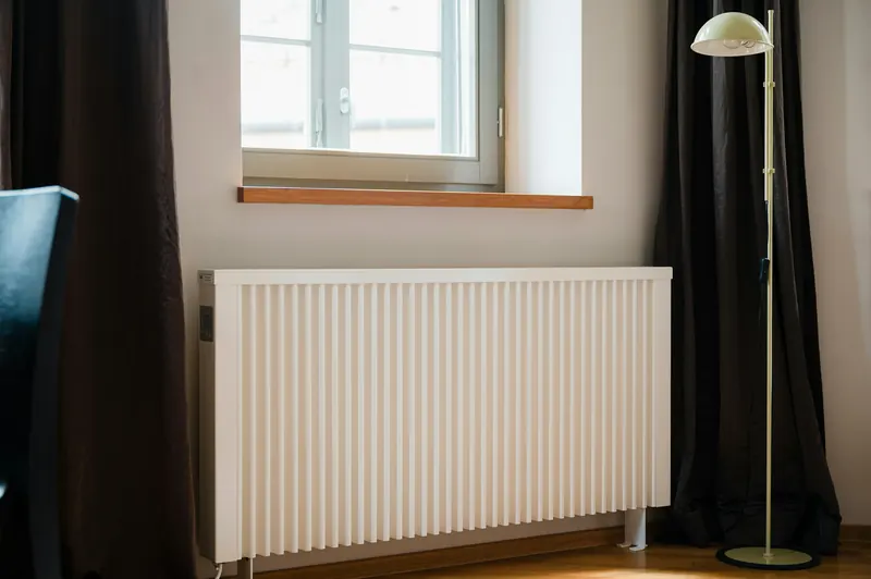 Radiateur blanc sous une fenêtre à rideaux sombres, à côté d'un lampadaire
