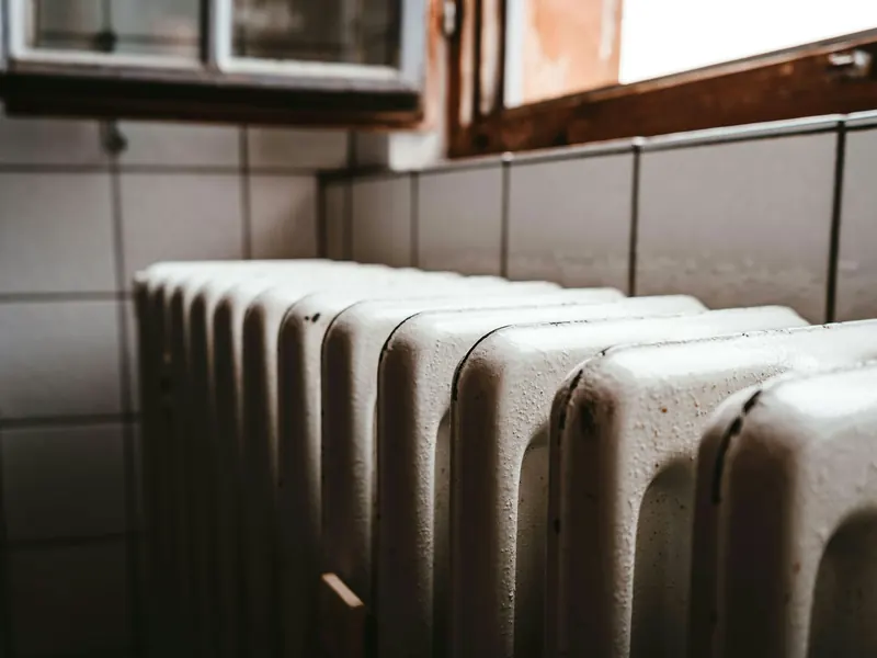 Radiateur en fonte blanc sous une fenêtre en bois, contre un mur carrelé