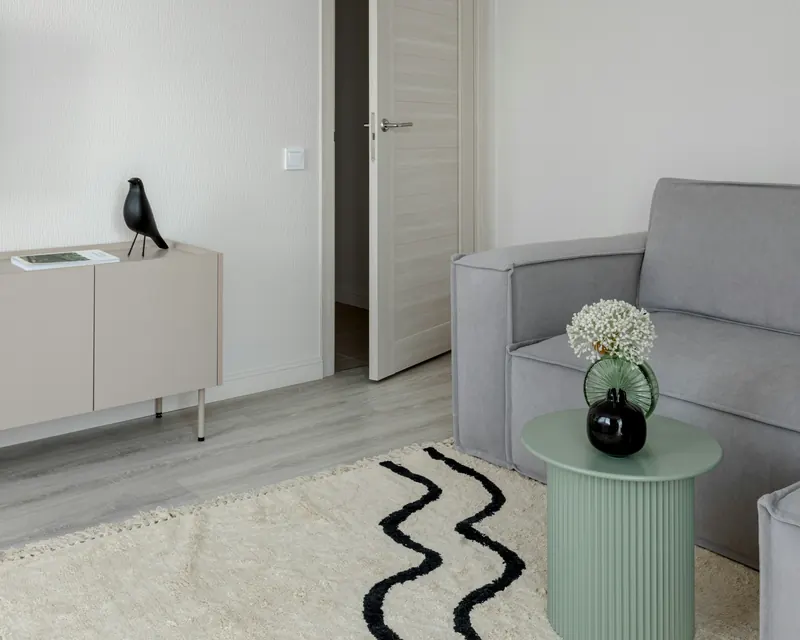 Salon minimaliste aux murs blancs, fauteuil gris, tapis clair et guéridon vert d'eau
