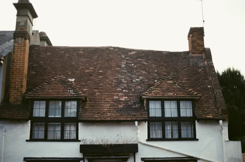 Vieille maison à toit de petites tuiles plates, deux lucarnes et deux cheminées de brique
