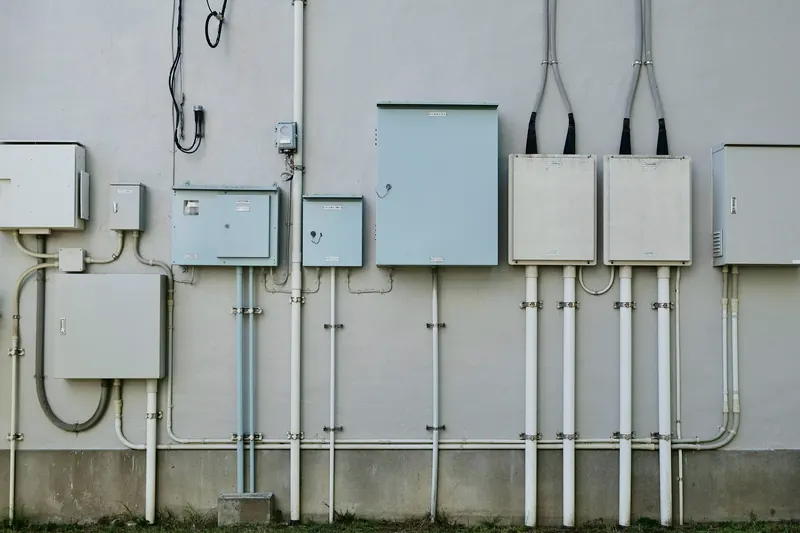 Boîtiers électriques gris et goulottes blanches alignés sur la façade d'un bâtiment