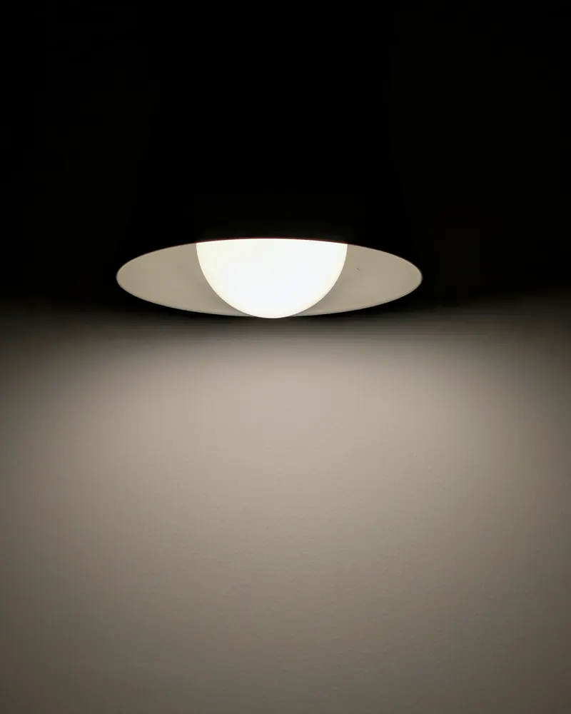 Suspension blanche allumée qui dessine un cône de lumière chaude sur un mur sombre
