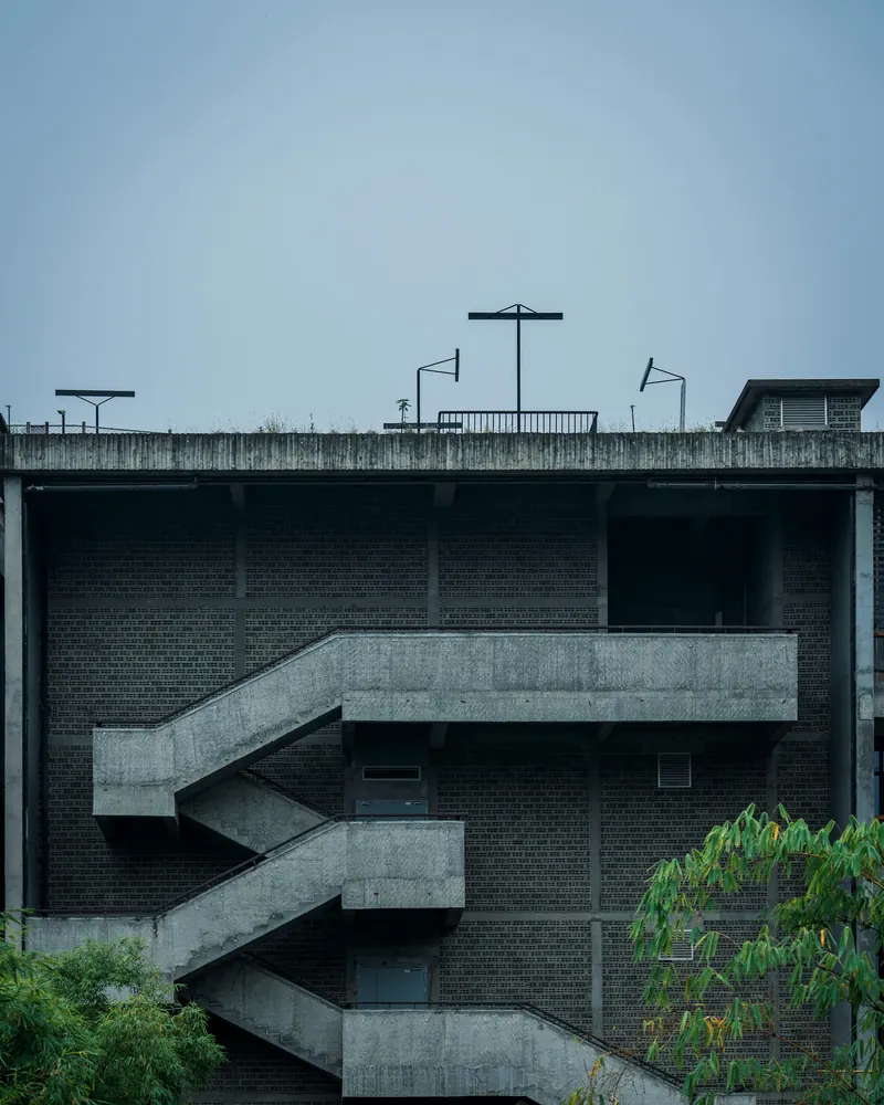 Escalier extérieur en béton aux volées en zigzag, accolé à une façade de briques grises sous un ciel bleu