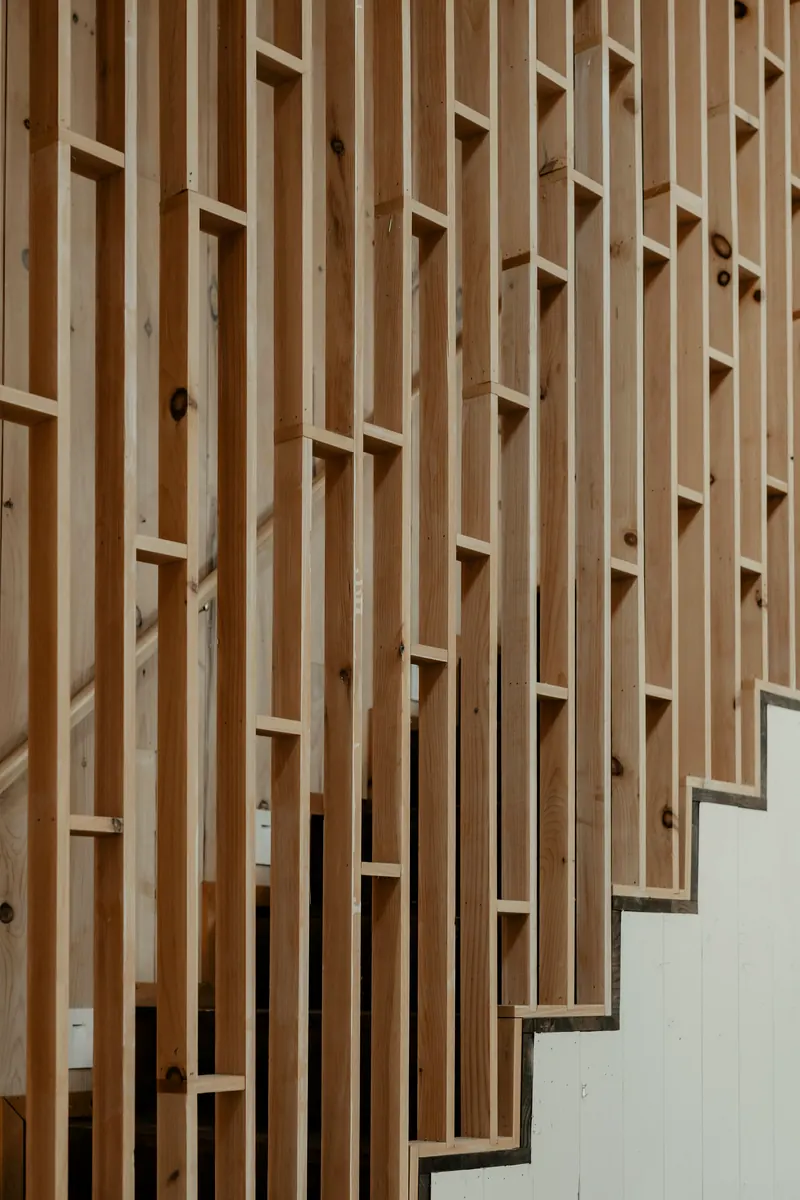 Claire-voie en lames de bois clair posées à la verticale le long d'un escalier, avec leurs nœuds et leurs veines apparents