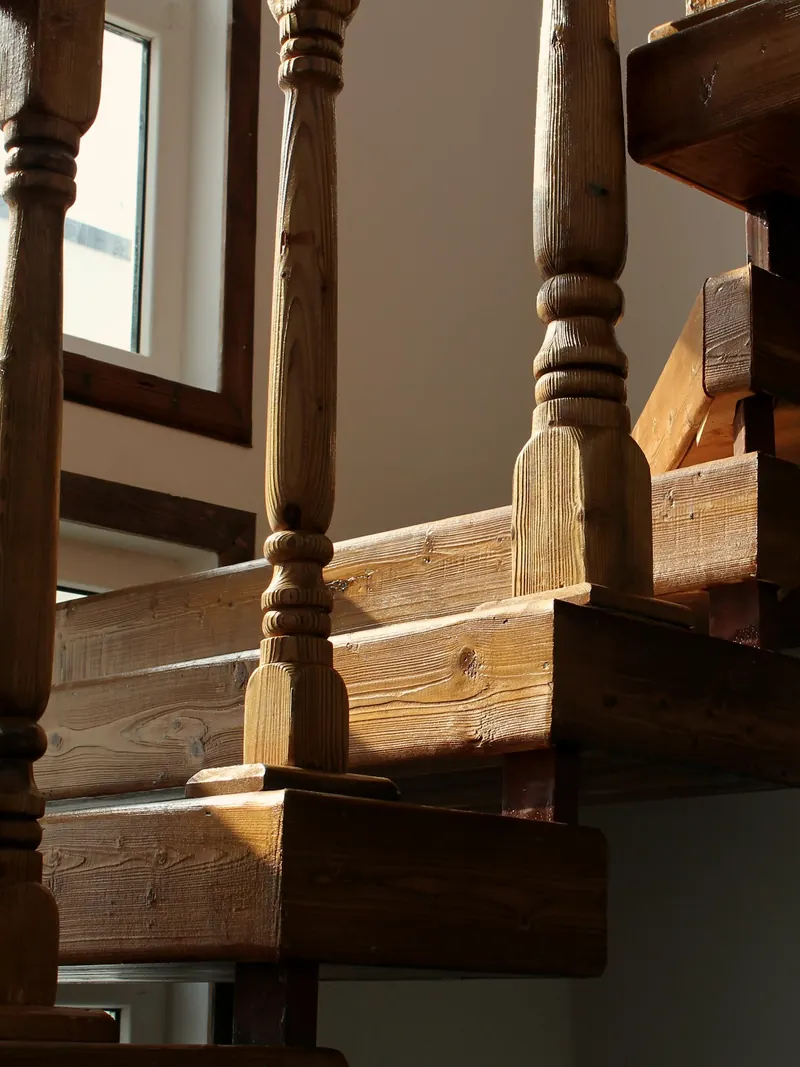 Escalier en bois massif vu d'en bas, avec ses balustres tournés et ses marches épaisses dans la lumière d'une fenêtre