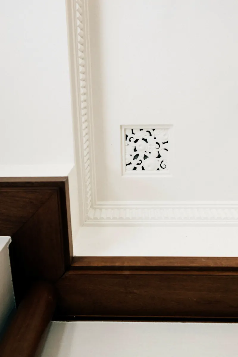 Détail d'une moulure blanche sculptée à l'angle d'un mur et d'un plafond, au-dessus d'une boiserie brune