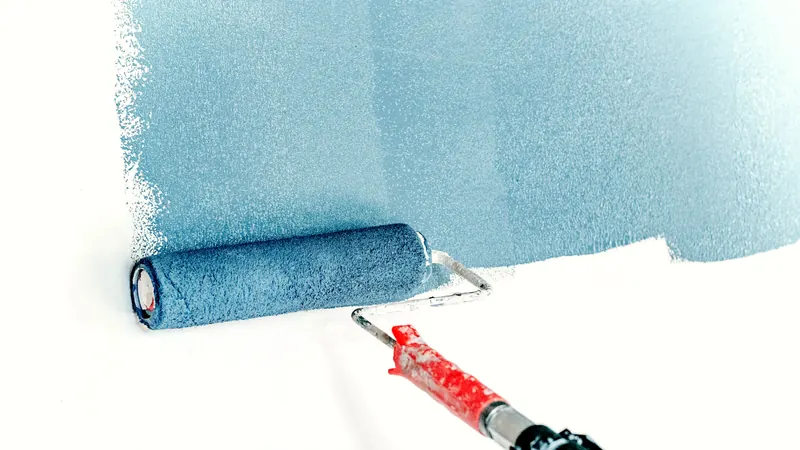 Rouleau à peinture passant une peinture bleue sur un mur blanc, avec la bande déjà peinte au-dessus
