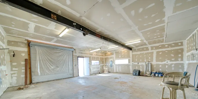 Pièce vide dont les murs et le plafond en plaques de plâtre montrent leurs bandes de joint et leurs reprises d'enduit blanc