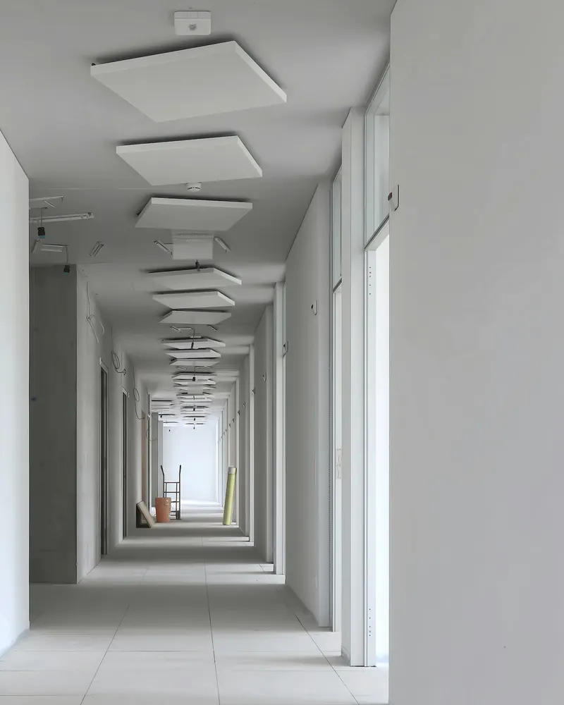 Long couloir aux cloisons blanches parfaitement lisses, plafond équipé de panneaux suspendus