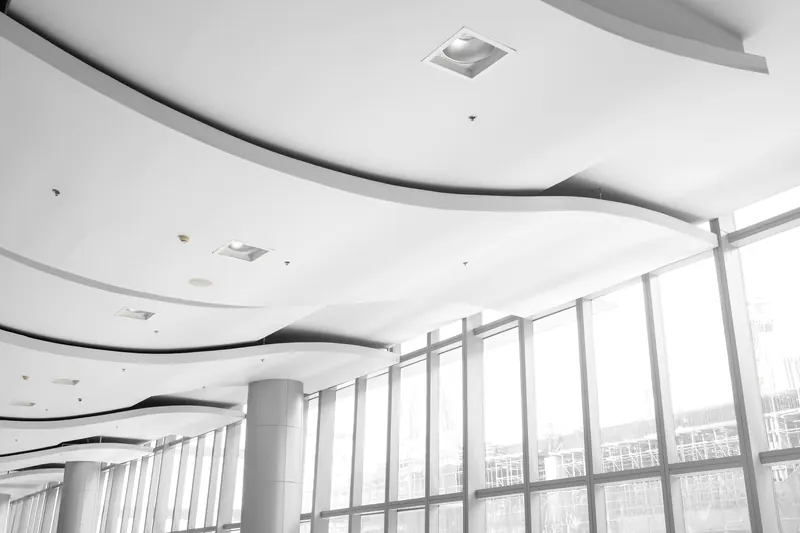 Faux plafond blanc en vagues, avec des spots encastrés, devant une grande façade vitrée
