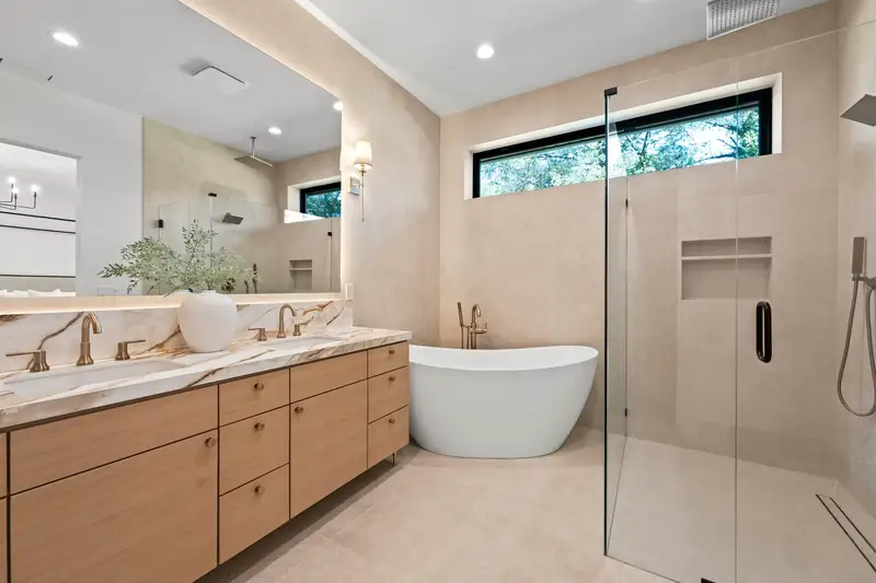 Salle de bains complète : double vasque en chêne et marbre veiné, baignoire îlot et douche vitrée aux carreaux beiges