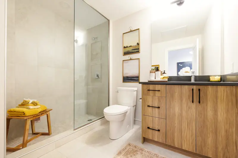 Grande douche fermée par une paroi de verre, carreaux clairs grand format, meuble en bois aux poignées noires