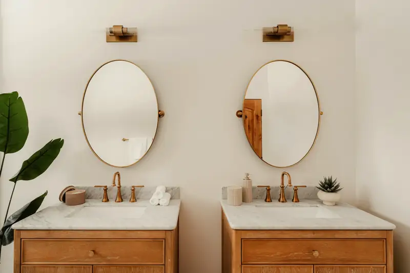 Deux meubles-vasques en chêne à plan de marbre, miroirs ovales à cadre laiton et appliques assorties