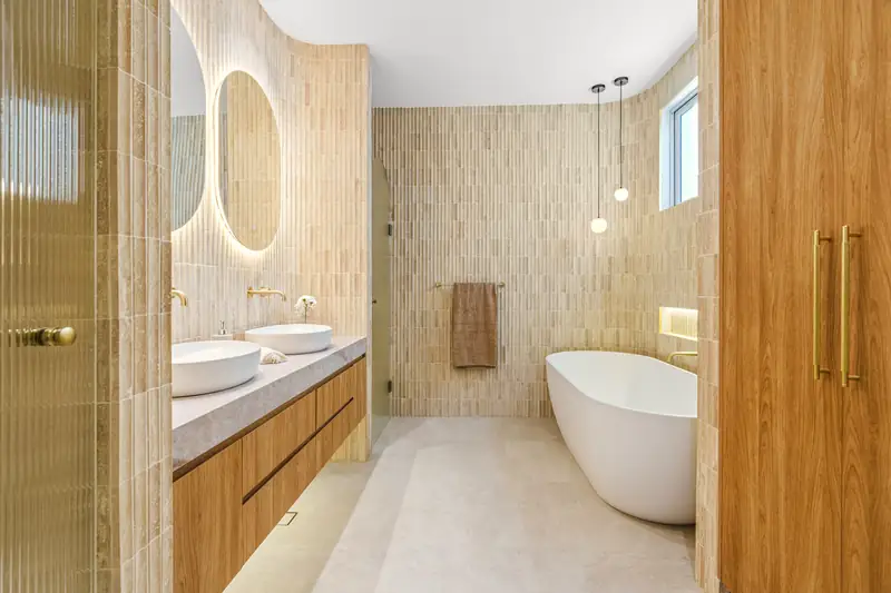 Salle de bains habillée de travertin clair en lamelles, double vasque sur meuble en chêne et baignoire îlot