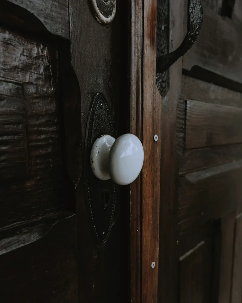 Bouton de porte en porcelaine blanche sur une platine de fer noir, au milieu d'une ancienne porte en bois sombre