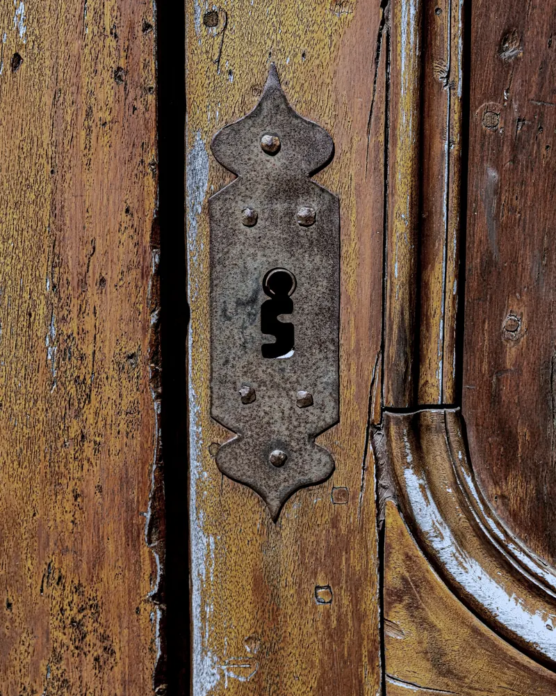 Gros plan sur l'entrée de clé d'une porte ancienne en bois, sous une platine de fer rouillé